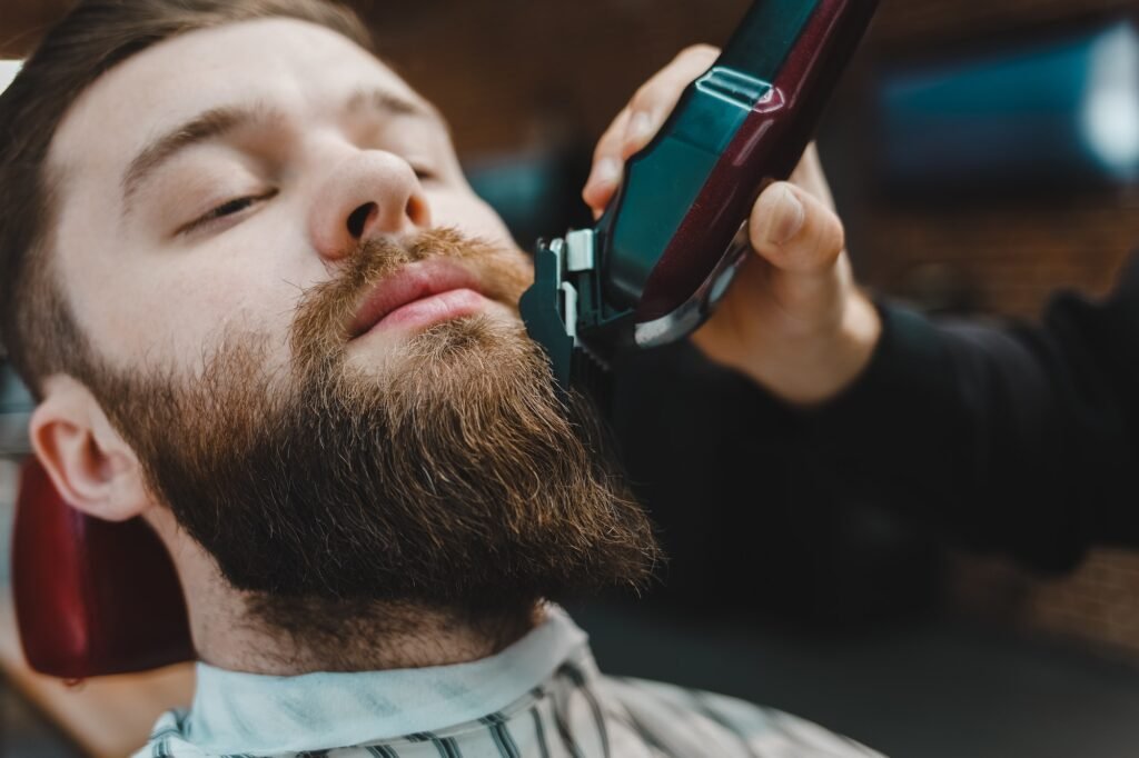 Barber master cuts a beard to a client close-up