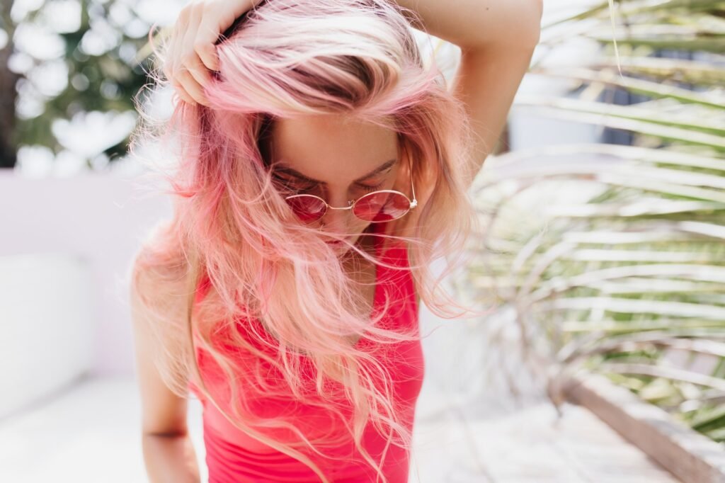 Dreamy woman with bronze skin playing with her pink hair. Outdoor photo of sensual female model in