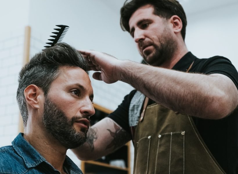 Barber combing hair to man in salon
