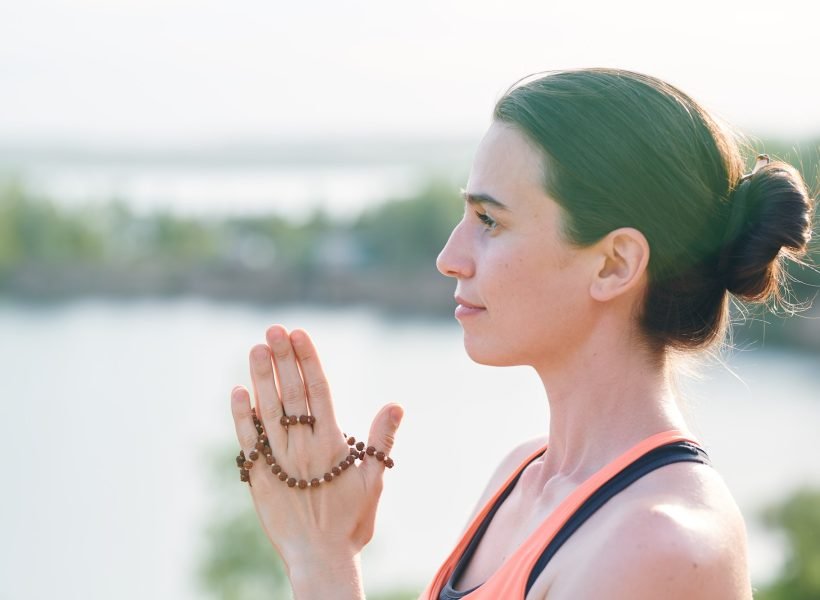 Side view of pensive young woman with hair bun holding mala beads in hands